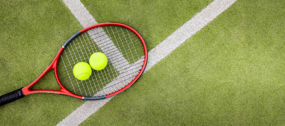 A red tennis racquet and two bright yellow tennis balls on a green court, illustrating spring pre-season gear preparation.